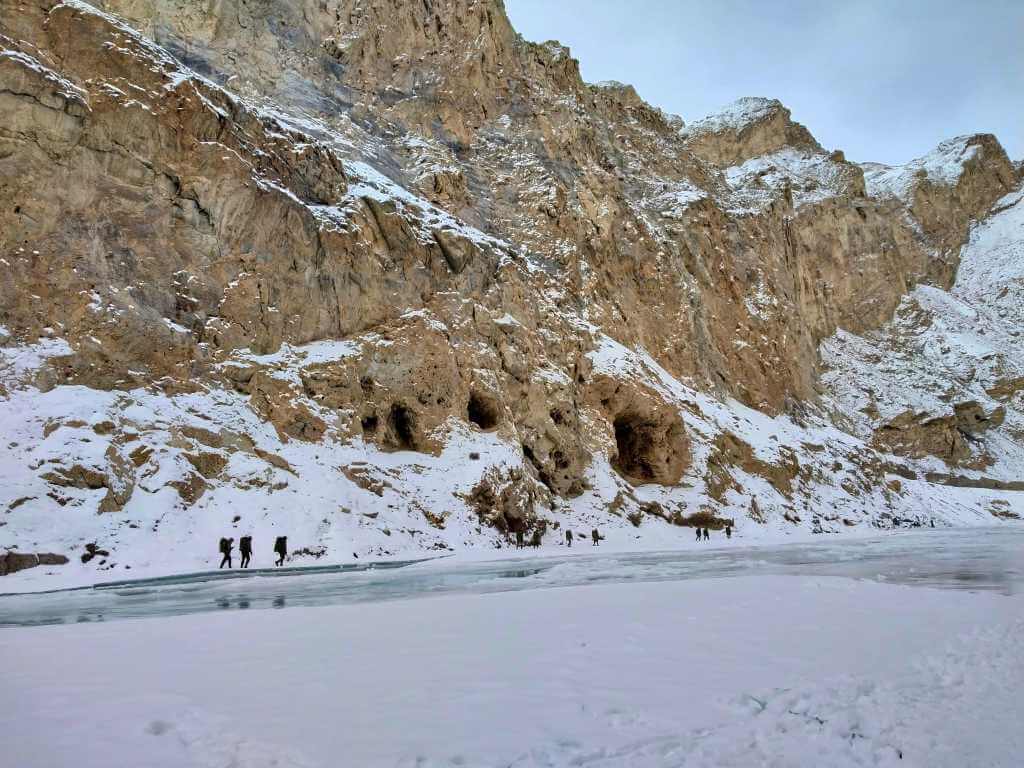 Trekkers walking under giant mountains during Chadar Trek Ladakh India